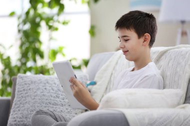 Evdeki kanepede tablet kullanan küçük çocuk.