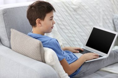 Evdeki kanepede dizüstü bilgisayar kullanan küçük çocuk.