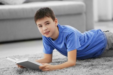 Küçük çocuk evde yerde kitap okuyor.
