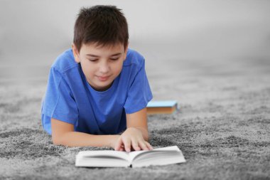 Küçük çocuk evde yerde kitap okuyor.
