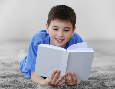 Küçük çocuk evde yerde kitap okuyor.