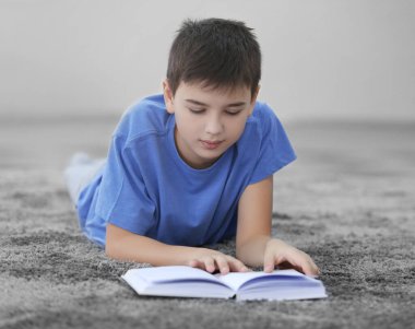 Küçük çocuk evde yerde kitap okuyor.