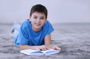 Küçük çocuk evde yerde kitap okuyor.