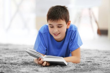 Küçük çocuk evde yerde kitap okuyor.