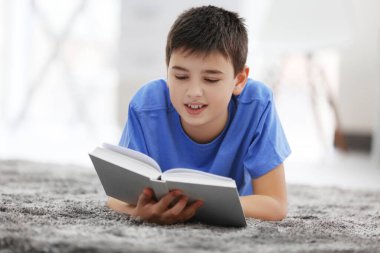 Küçük çocuk evde yerde kitap okuyor.