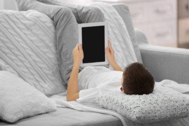 Evdeki kanepede tablet kullanan çocuk.