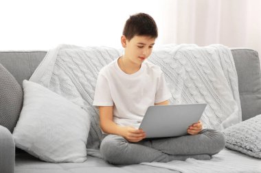 Çocuk evdeki kanepede dizüstü bilgisayar kullanıyor.