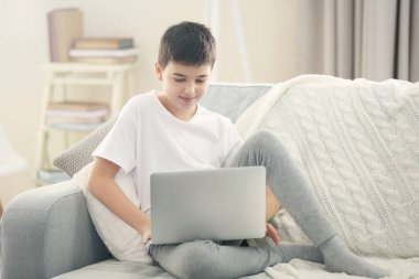 Çocuk evdeki kanepede dizüstü bilgisayar kullanıyor.