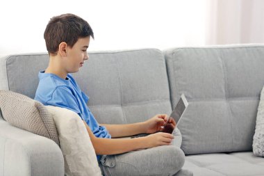 Çocuk evdeki kanepede dizüstü bilgisayar kullanıyor.