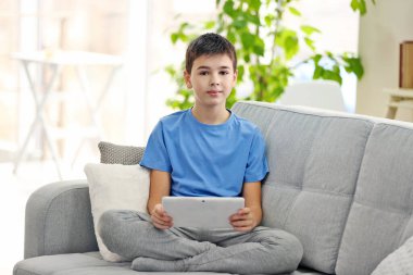 Evdeki kanepede oturan tabletli çocuk.
