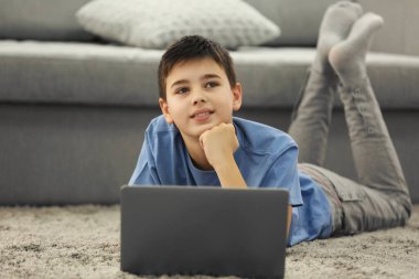 Evdeki halıda dizüstü bilgisayar kullanan bir çocuk.