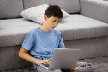 Evdeki halıda dizüstü bilgisayar kullanan bir çocuk.
