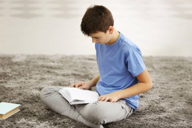 Çocuk evde yerde kitap okuyor.