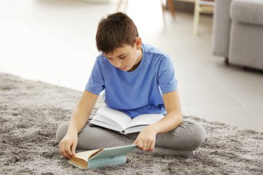 Çocuk evde yerde kitap okuyor.