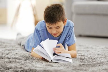 Çocuk evde yerde kitap okuyor.