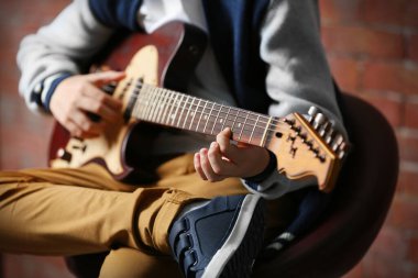 Tuğla duvar arkasında gitar çalan sevimli bir çocuk.