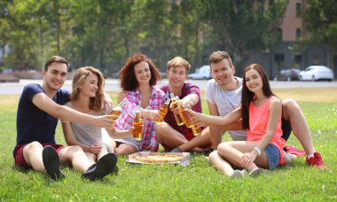 Pizza ve birayla çimenlerde oturan genç arkadaşlar.