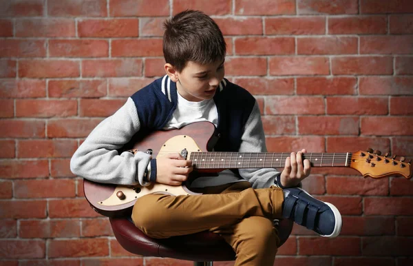 かわいい男の子演奏ギターでレンガの壁の背景 — ストック写真