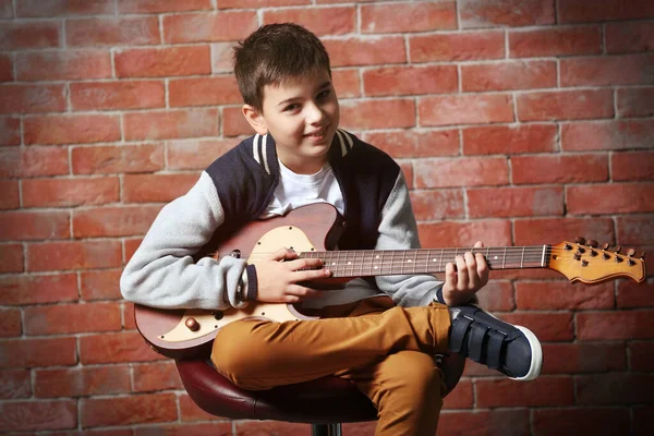 かわいい男の子演奏ギターでレンガの壁の背景 — ストック写真