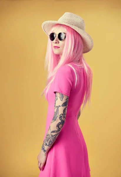 漂亮的年轻女子 戴着粉色假发 头戴黄底帽 戴着太阳镜 身上有纹身 — 图库照片