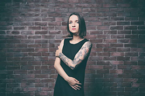 Beautiful young woman with tattoo posing on brick wall background