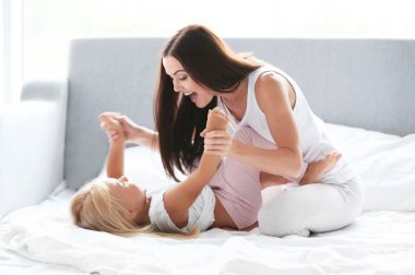 Mutlu anne yatakta kızıyla oynuyor.