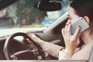 Cep telefonlu bir kadın araba kullanıyor.