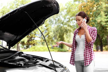 Cep telefonu ve yolda bozuk arabası olan bir kadın.