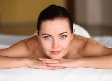 Sırtını ovuşturup masaj masasına uzanan genç bir kadın.