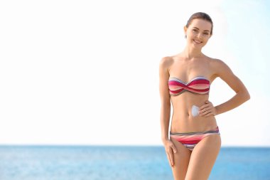 Genç bir kadın sahilde vücuduna güneş kremi sürüyor.