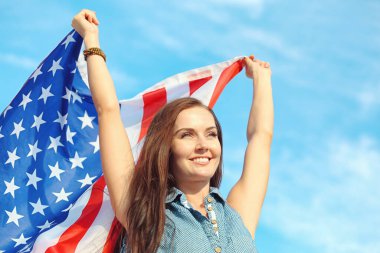 Gökyüzünde Amerikan bayrağı taşıyan mutlu genç bir kadın.