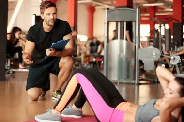 Spor salonunda antrenörle egzersiz yapan genç atletik bir kadın.