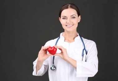 Steteskoplu, kalbi olan, koyu arkaplanda bir kadın doktor.