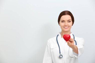 Steteskop tutan, kalbi hafif arka planda olan kadın bir doktor.