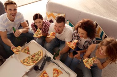 Arkadaşlar kanepede oturup lezzetli pizzaları yiyorlar.
