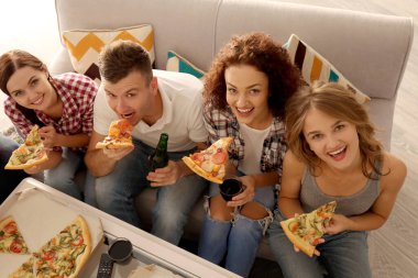 Arkadaşlar kanepede oturup lezzetli pizzaları yiyorlar.