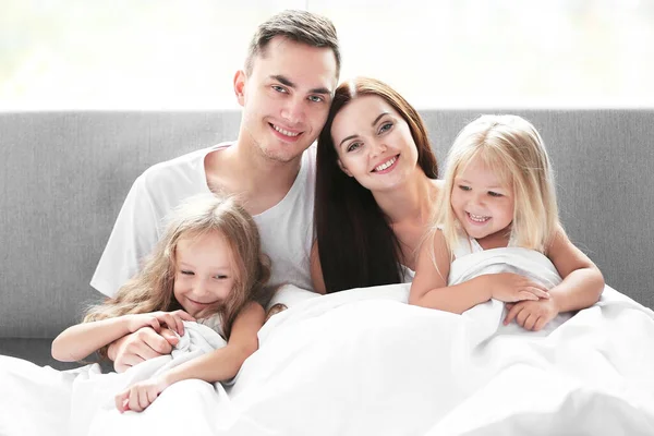 Happy parents with daughters under blanket in bed