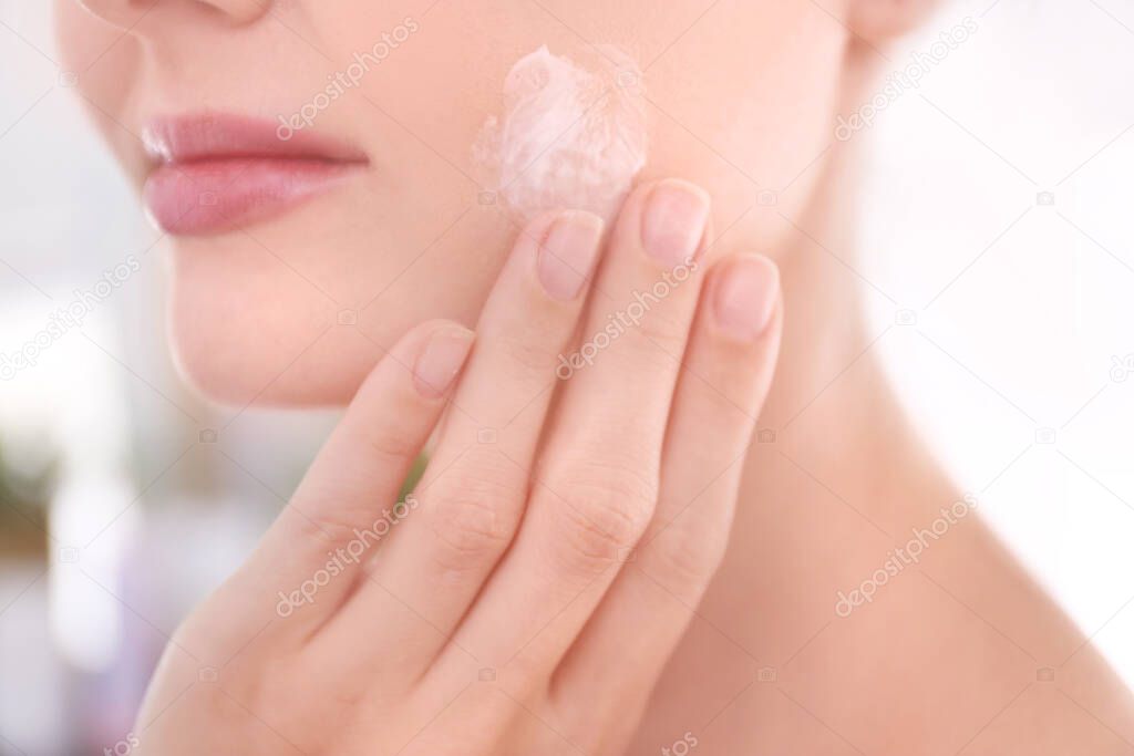 Beautiful young woman applying cream onto face