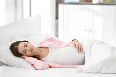 Genç hamile kadın beyaz yatakta uyuyor.