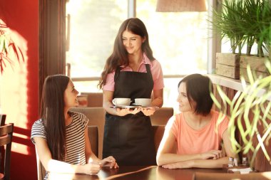 Genç garson neşeli kadınlara kafede kahve getiriyor