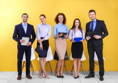 Sarı duvarda iş görüşmesi için bekleyen bir grup insan var.