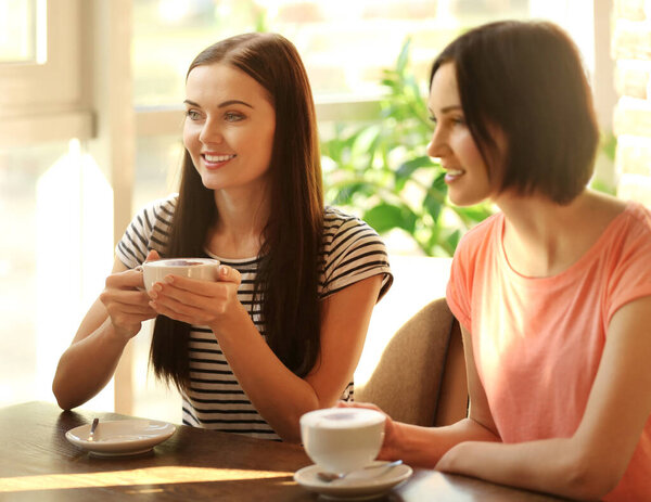 Cheerful young women drinking coffee in cafe on sunny day