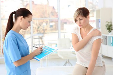 Ortopedist klinikteki orta yaşlı kadını muayene ediyor.