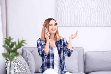 Evdeki koltukta otururken cep telefonu kullanan genç bir kadın.