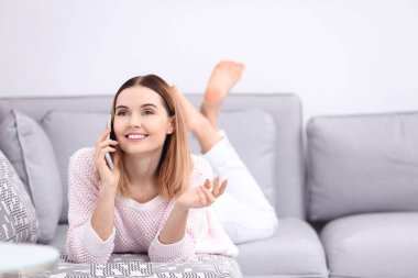 Evdeki kanepede uzanırken cep telefonu kullanan genç bir kadın.