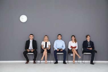 Gri duvar arkasında iş görüşmesi için bekleyen bir grup insan.