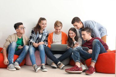 Modern cihazlarla beyaz duvara yakın oturan genç grup