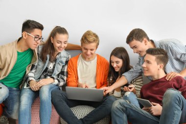 Modern cihazlarla beyaz duvara yakın oturan genç grup