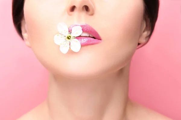 色の背景に唇の間に花を持つ美しい若い女性 — ストック写真