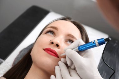 Profesyonel dövme ustası kuaförde dudaklarına kalıcı makyaj uyguluyor.